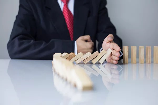Business person stopping dominos from falling, signifying the importance of a business continuity plan.