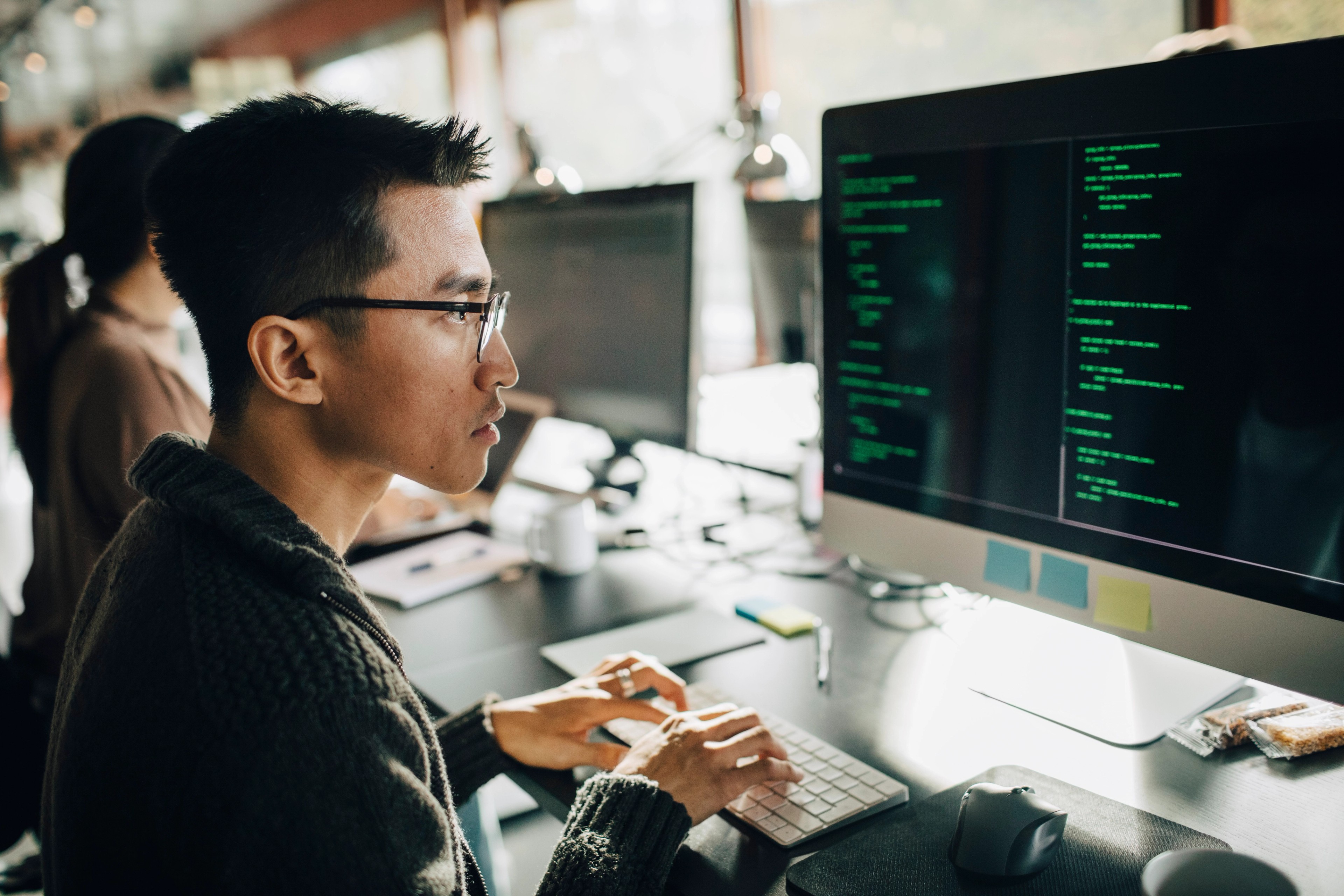 Side view of focused male developer coding on computer while sitting at working at office