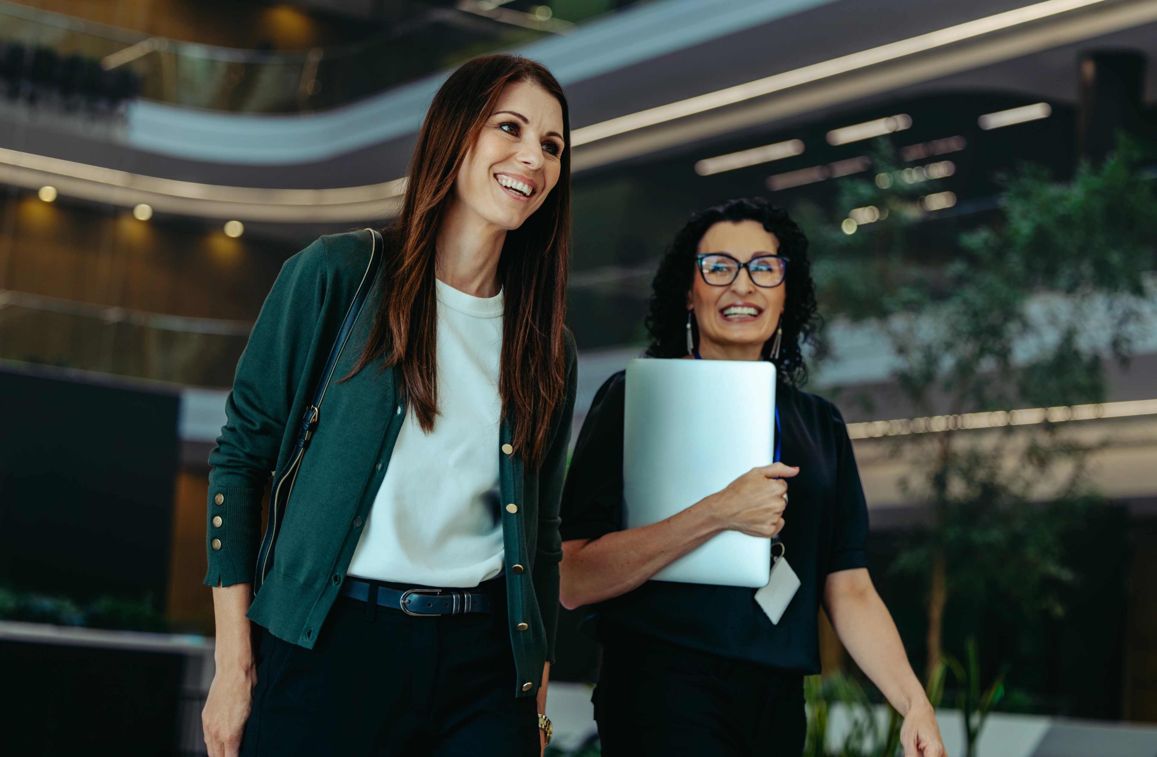 Two female professionals in a corporate setting, walking through a modern building.