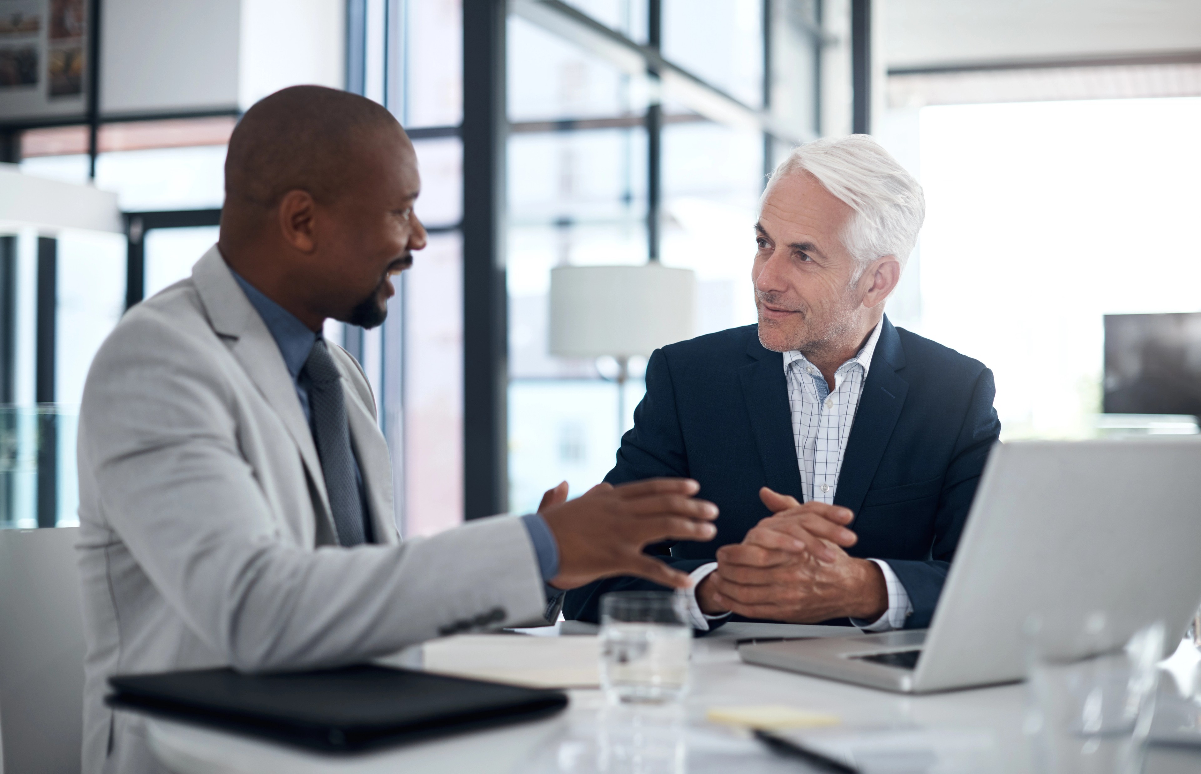 Two businessmen talking over a laptop display.