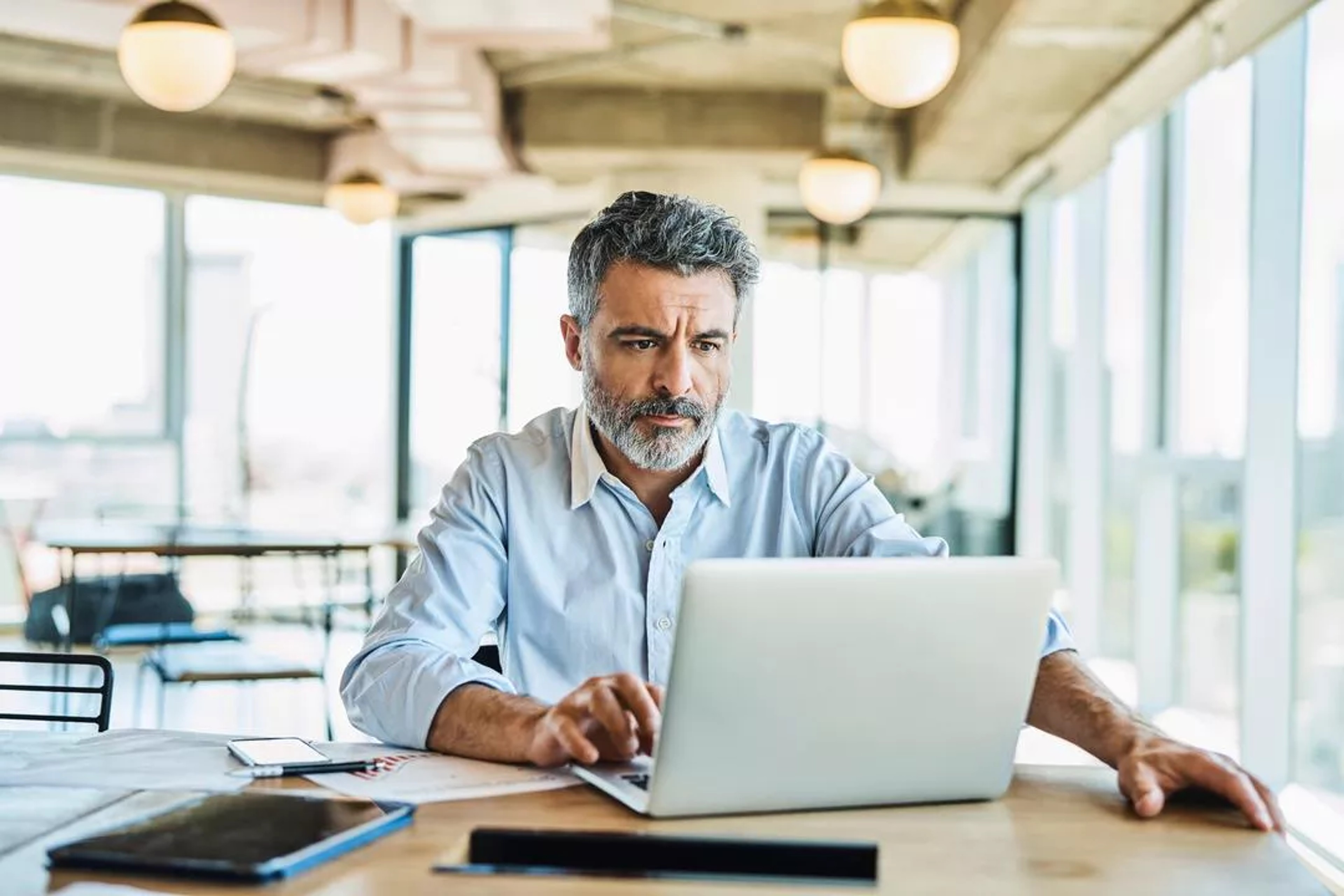 Man sits at a desk in an office, looking at a laptop