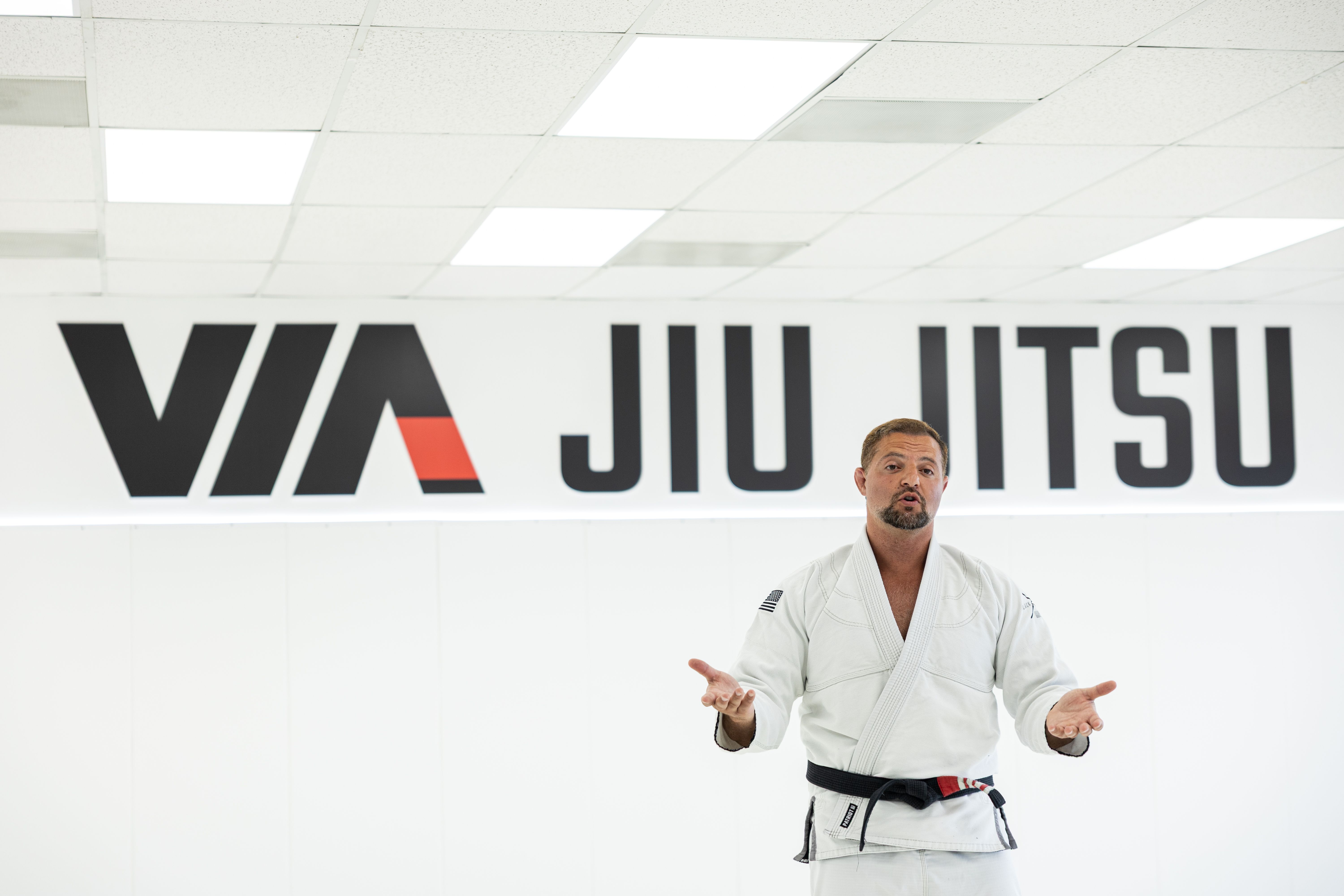 Instructor speaking in front of the Via Jiu Jitsu wall logo