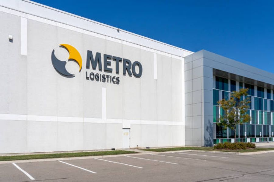 Exterior of a modern warehouse building with âMetro Logisticsâ signage, featuring a large industrial facility and parking lot under a clear blue sky