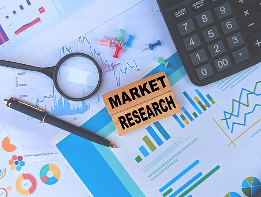 A flat lay of market research materials including printed charts, a magnifying glass, calculator, pen, colorful pins, and wooden blocks spelling out market research