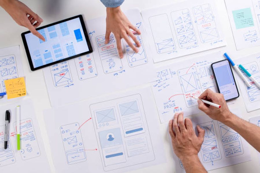A team working on UX wireframes and mobile app layouts spread across a table, representing the process of planning and optimizing the user experience to reduce friction and improve conversion rate.