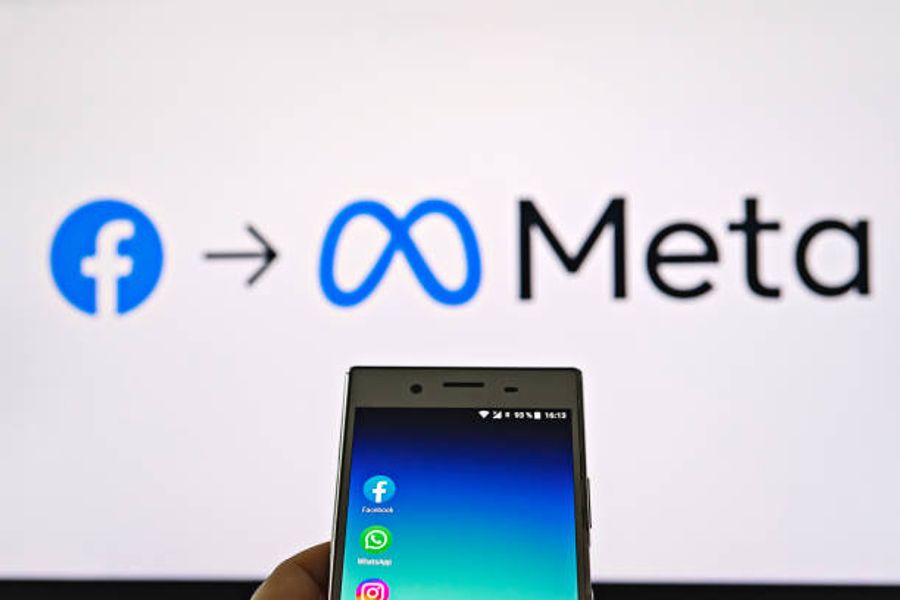Smartphone displaying social media apps in front of a screen showing the Facebook logo transitioning to the Meta logo, representing the company’s rebrand from Facebook to Meta.