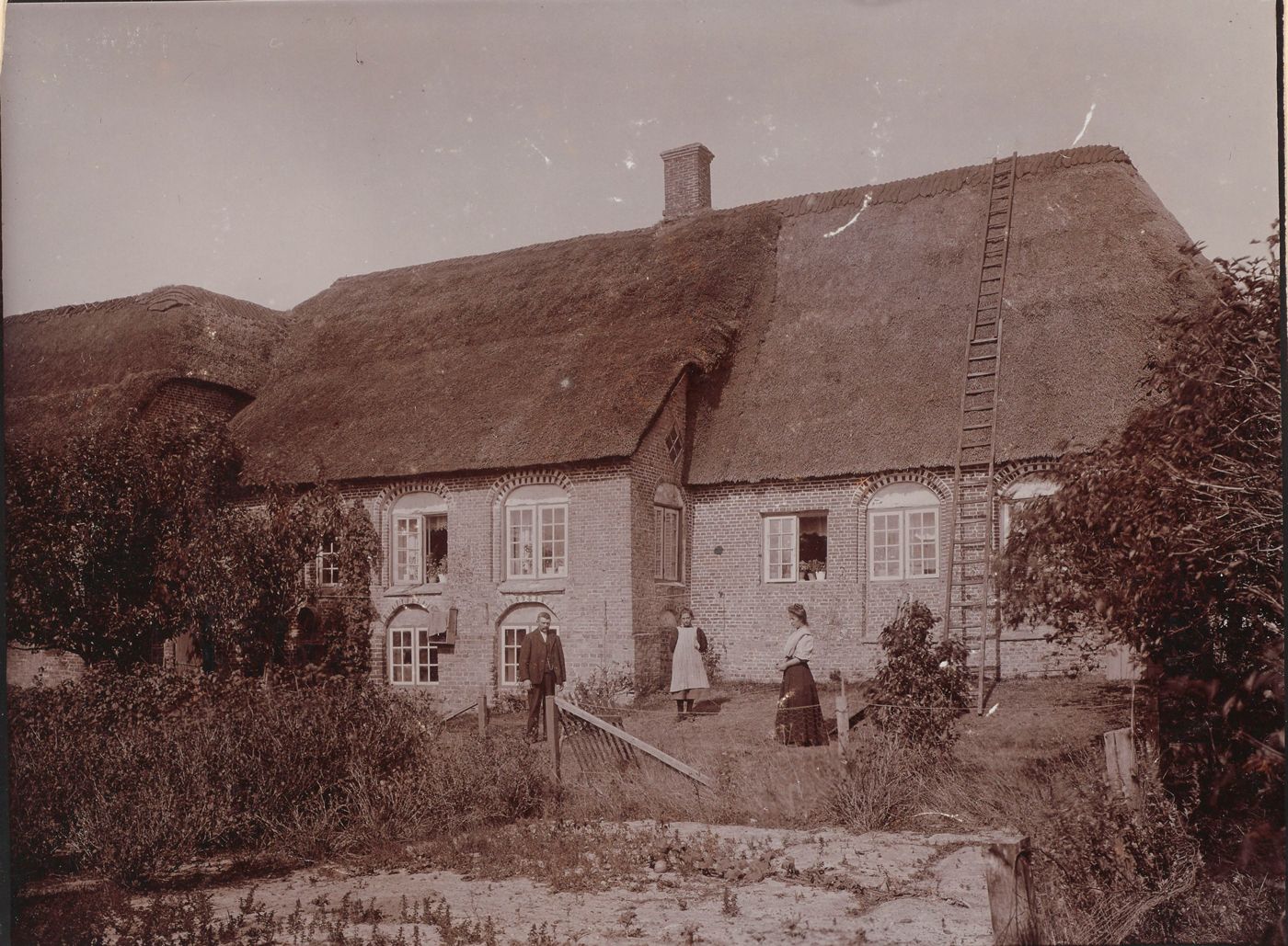 Historisk foto af Kommandørgårdens facade med stråtag, murstensværk og beboere foran huset