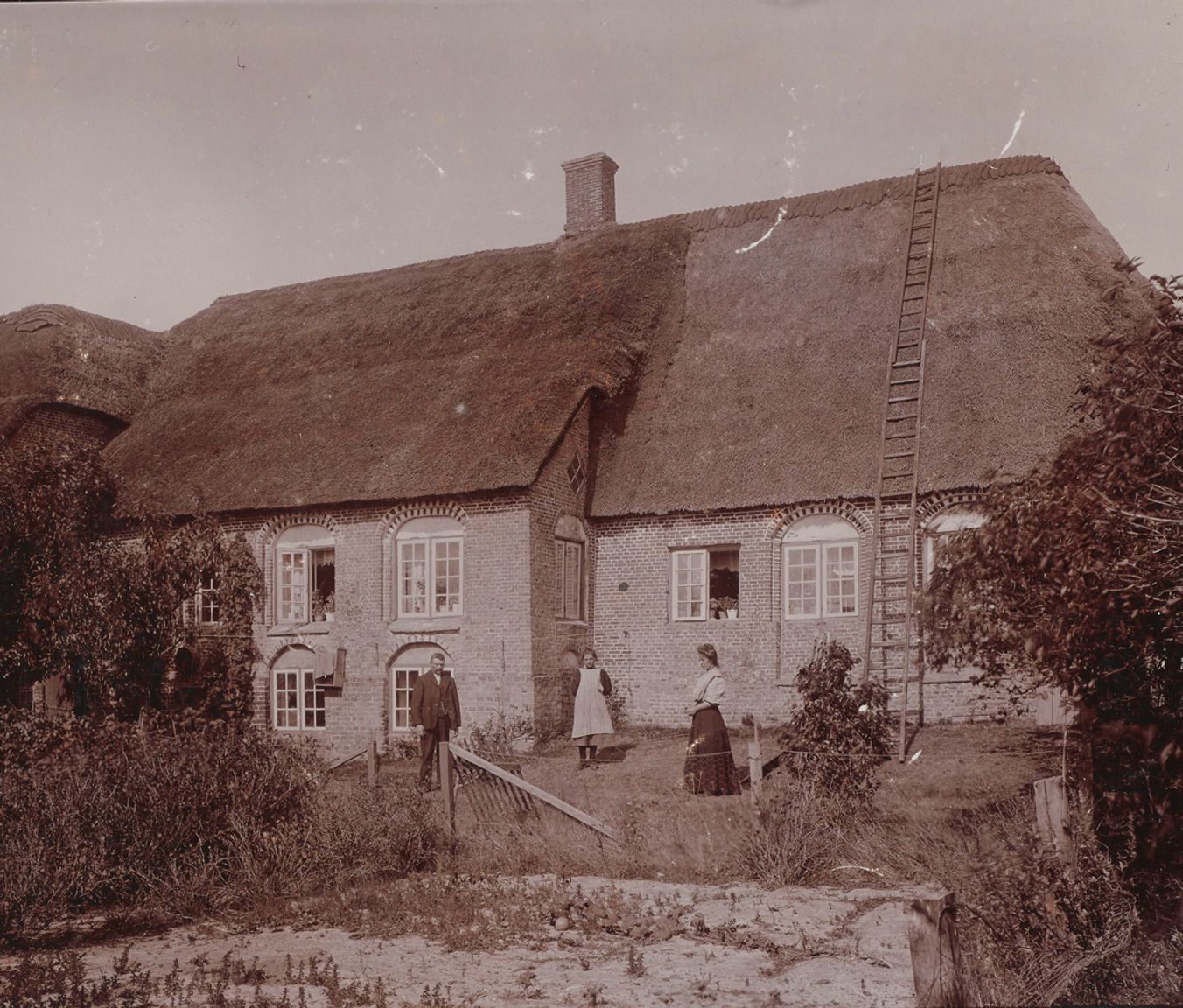 Historisk foto af Kommandørgårdens facade med stråtag, murstensværk og beboere foran huset
