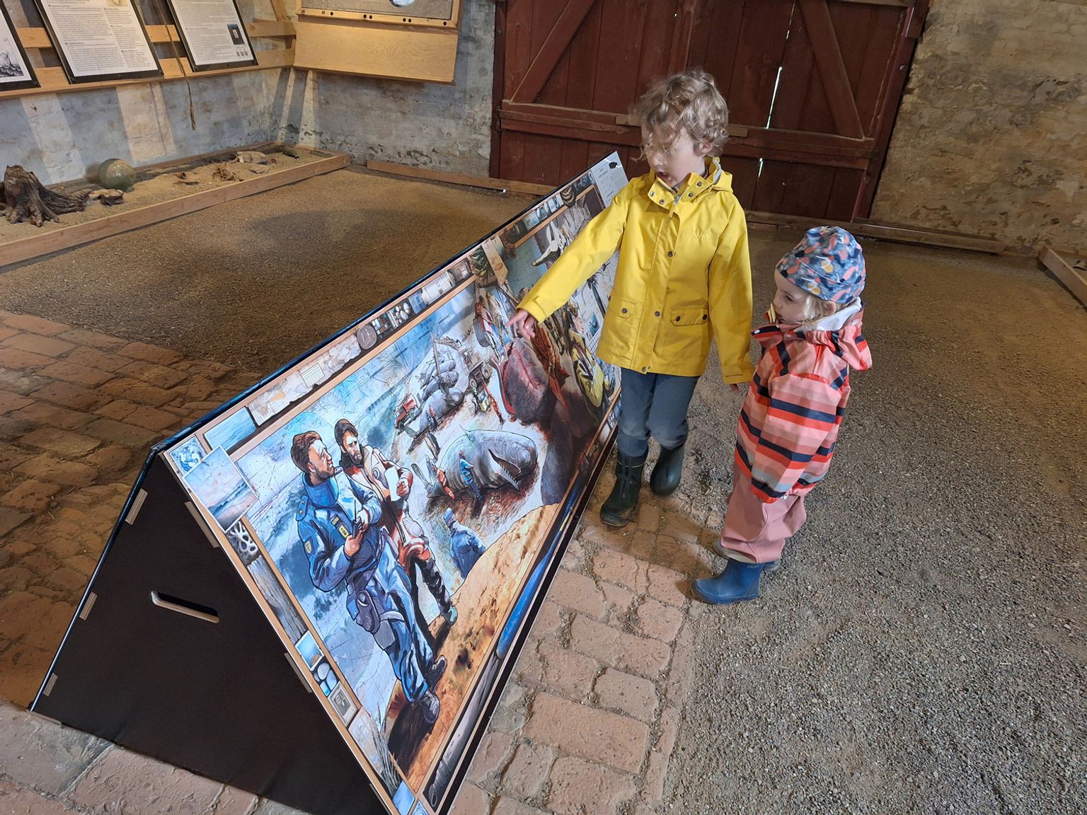 To børn udforsker en illustreret formidlingstavle om kaskelotstranding i Kommandørgårdens lade