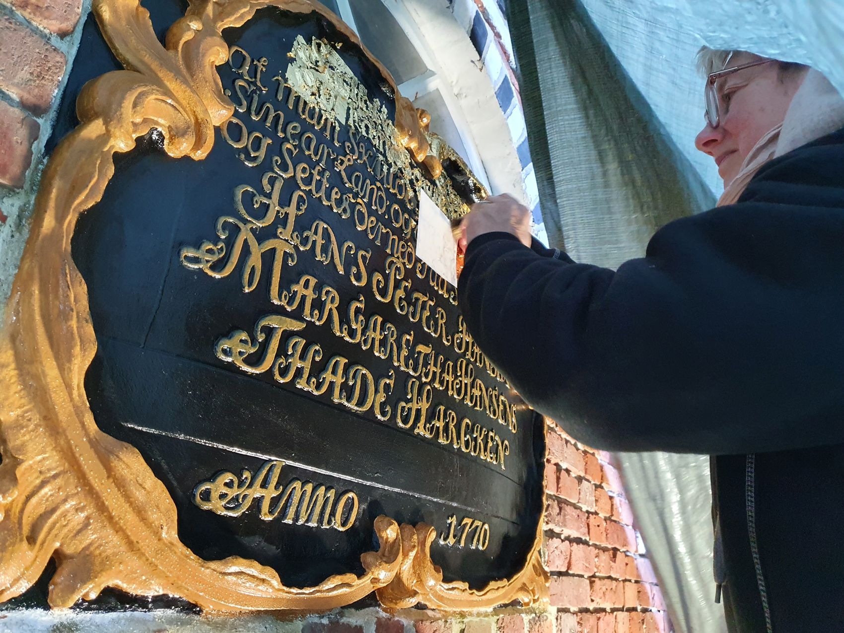 Konservator udfører bevaringsarbejde på Kommandørgårdens historiske indskriftstavle med guldskrift fra 1770