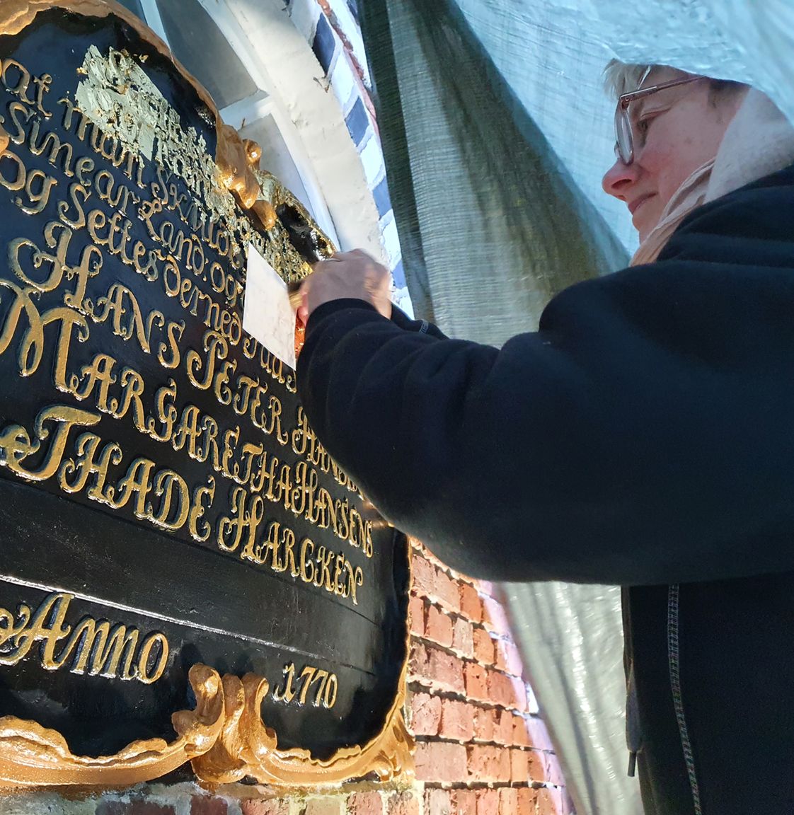 Konservator udfører bevaringsarbejde på Kommandørgårdens historiske indskriftstavle med guldskrift fra 1770