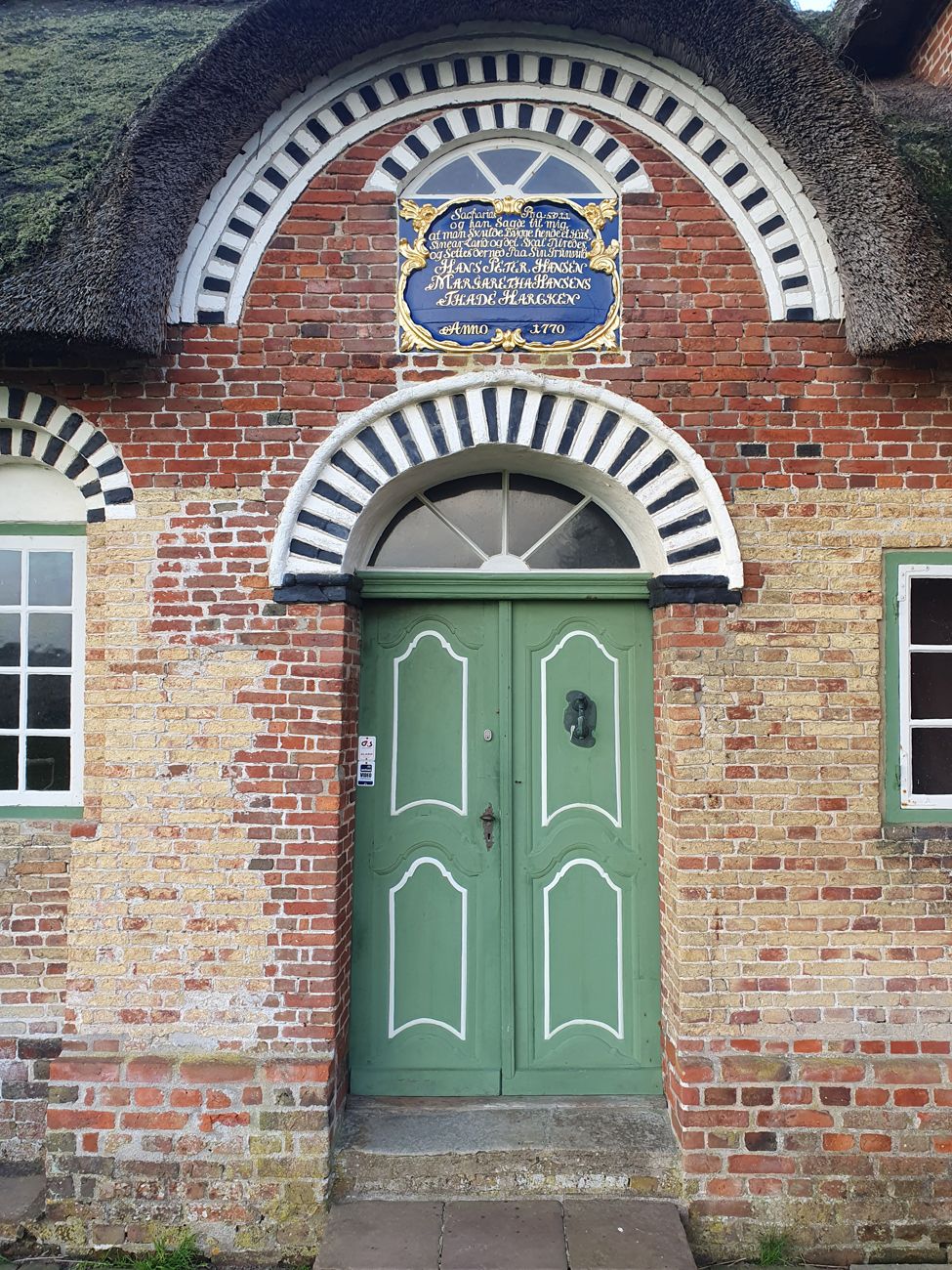 Kommandørgårdens grønne hoveddør med dekorativ muret bue og historisk indskriftstavle over dørpartiet
