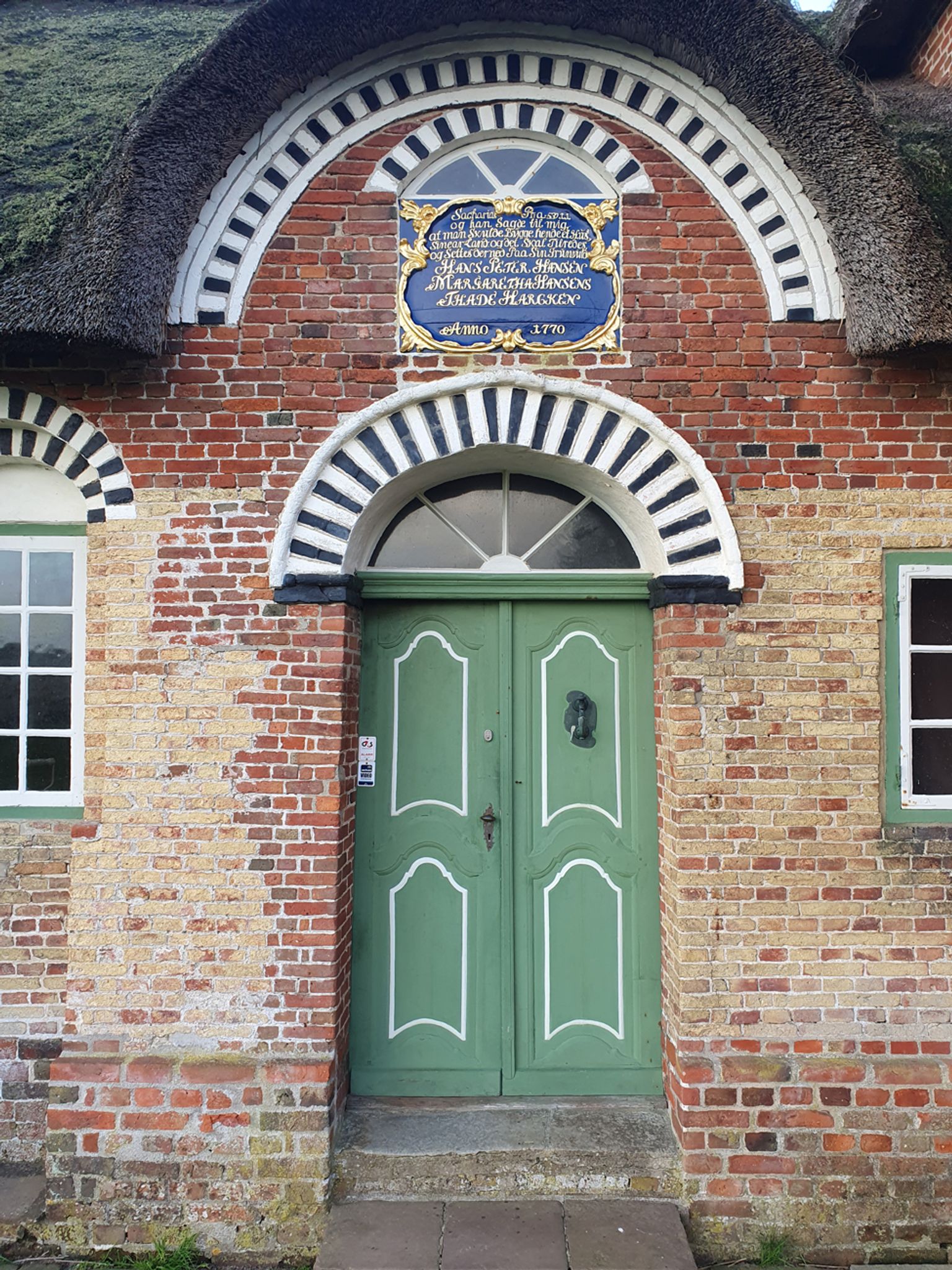 The Sea Captain's House green front door with decorative brick arch and historic inscription plaque above the entrance