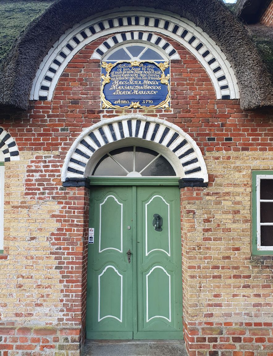 Kommandørgårdens grønne hoveddør med dekorativ muret bue og historisk indskriftstavle over dørpartiet