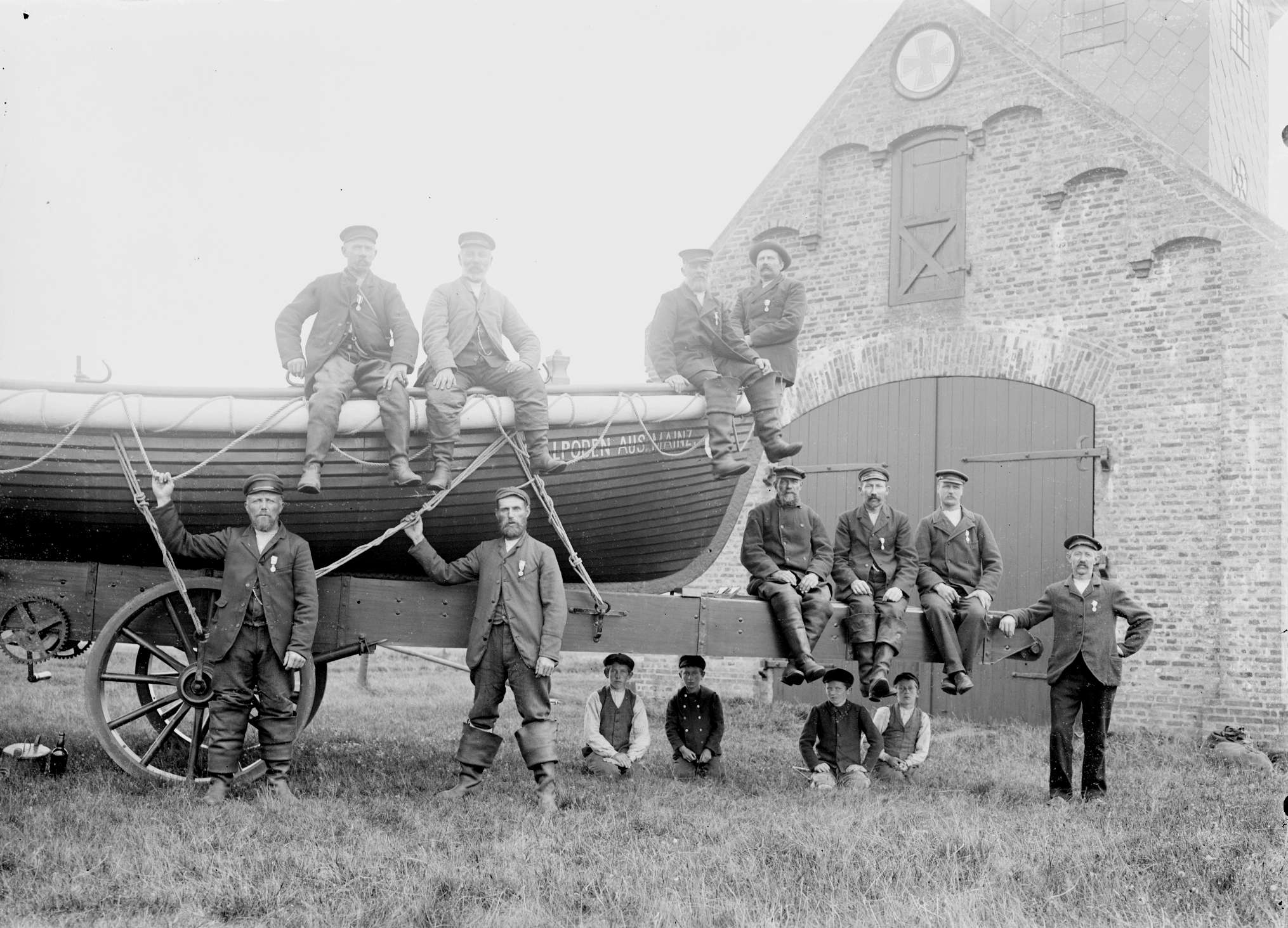 Historisk foto af redningshold med redningsbåd på vogn foran redningsstation – mænd og drenge i uniform. Kilde: arkiv.dk