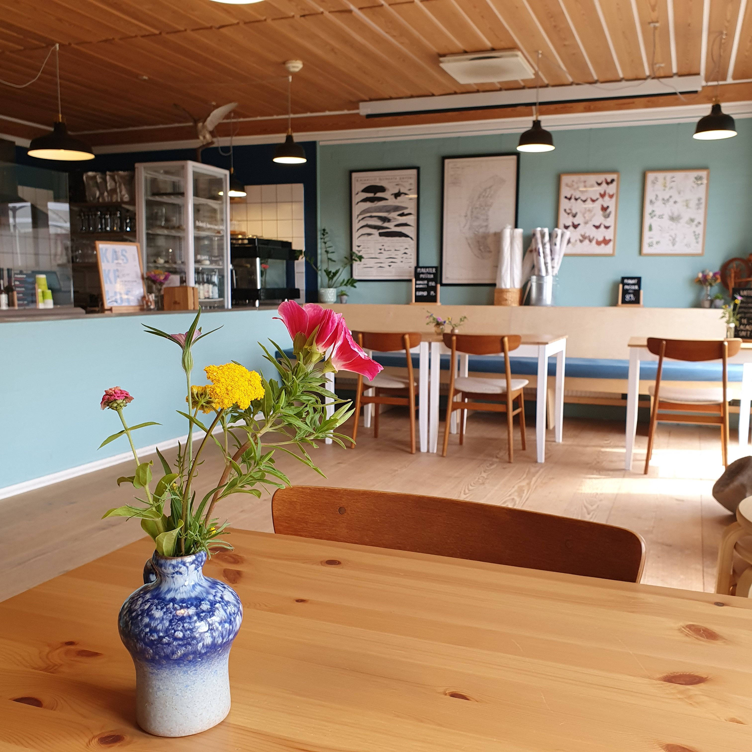 Kommandørgårdens café med træborde, friske blomster i vase og naturplakater på de lyseblå vægge