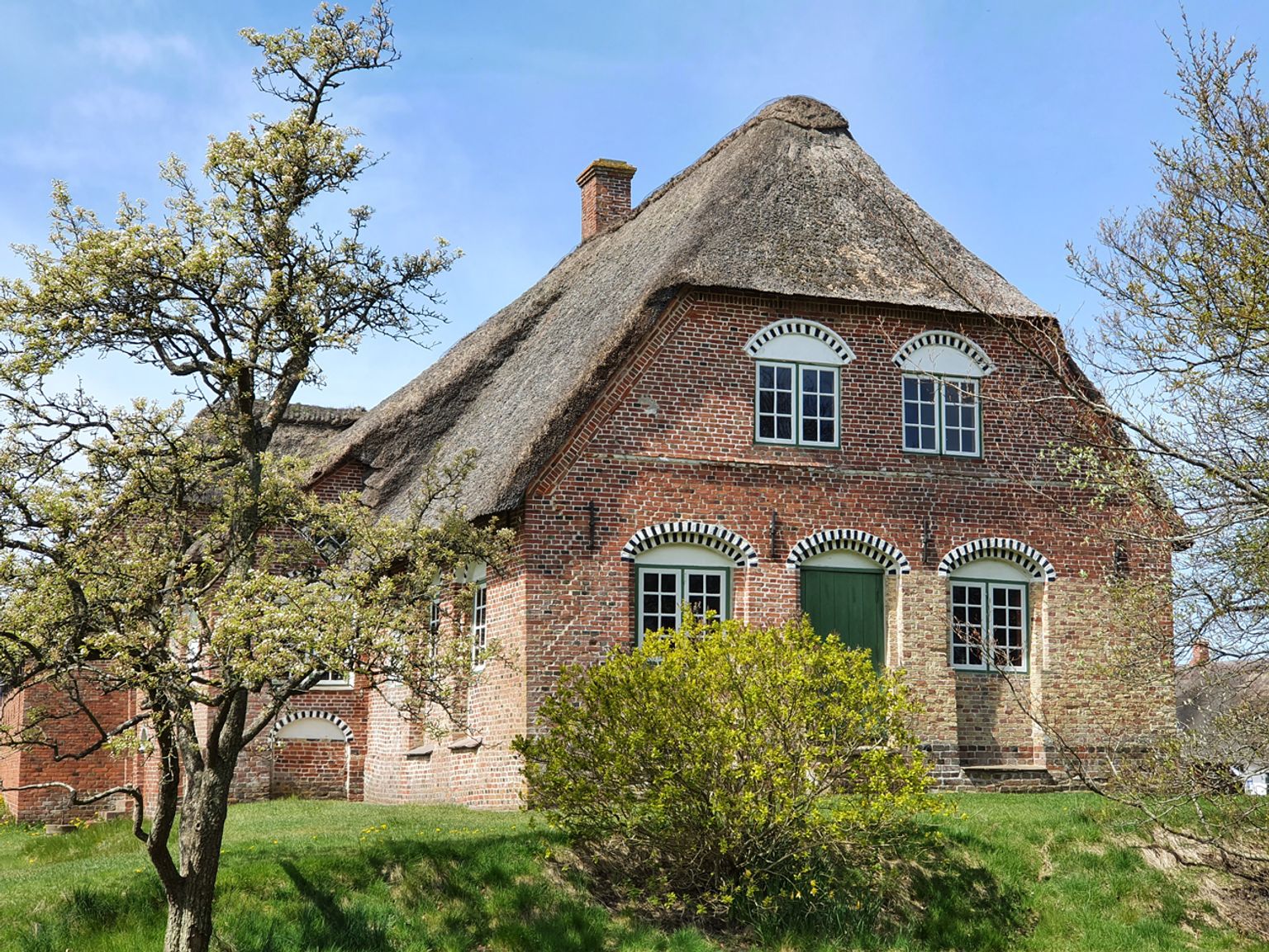 Kommandørgårdens facade i forårslys med stråtag, karakteristiske murede buer over vinduer og grøn hoveddør