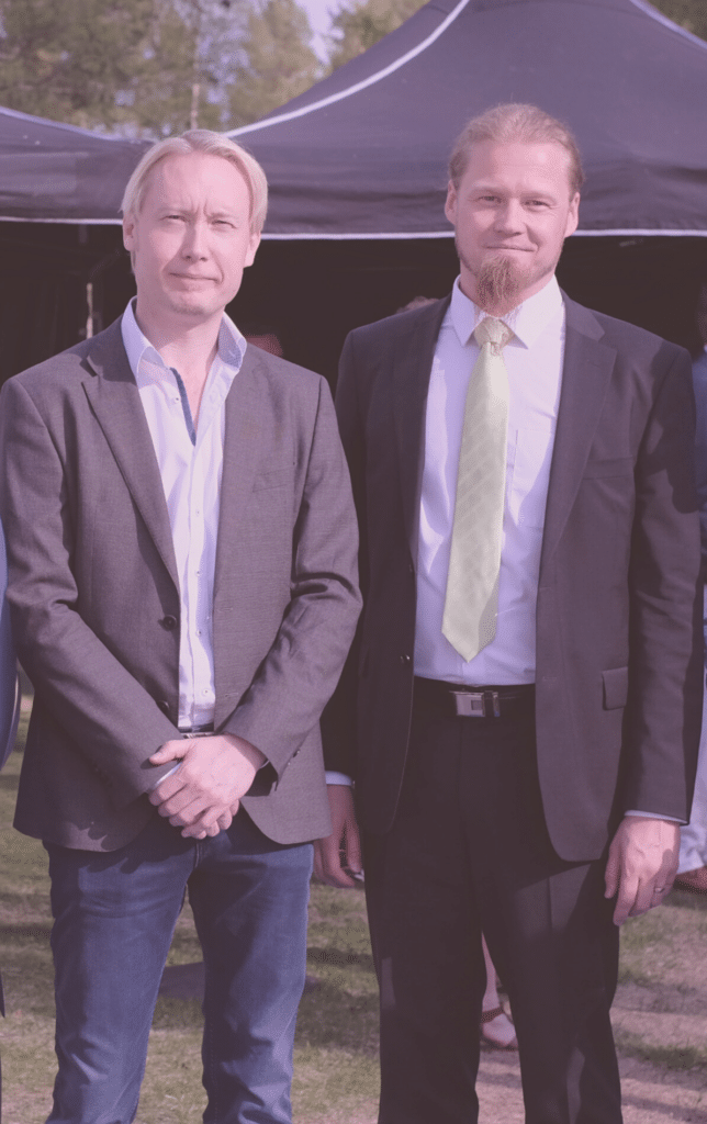 Jukka Katajaharju and Toni Piirainen at tha party, smiling. They both are wearing suits, behind them there's a big tent.