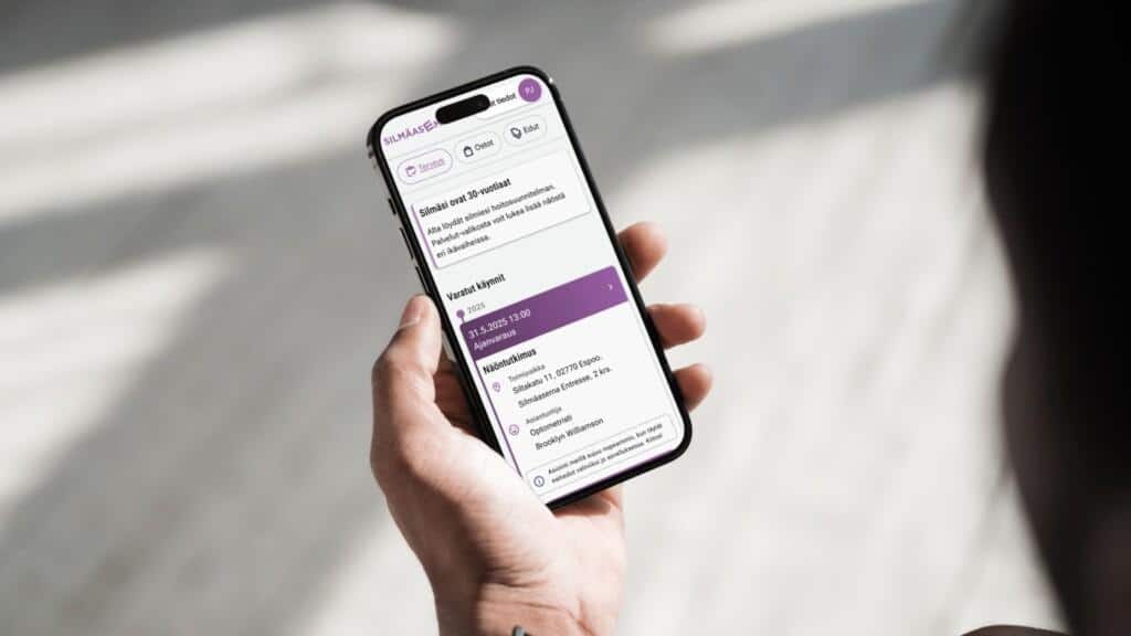 Käsi pitelee älypuhelinta, jossa on avoinna OmaSilmä-sovellus ja näkymä tulevasta näöntutkimusajasta sekä käyttäjän tiedoista.