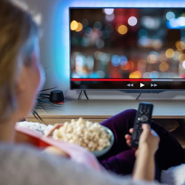 Person watching Netflix streaming service at home on a TV, holding a remote and popcorn, illustrating the user experience of the platform.
