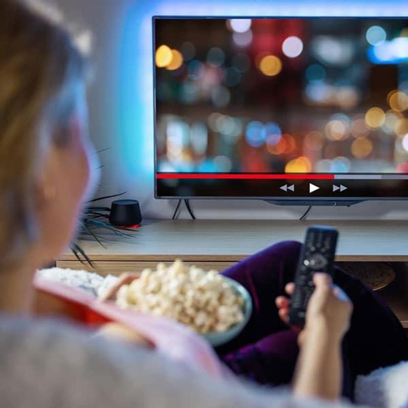 Person watching Netflix streaming service at home on a TV, holding a remote and popcorn, illustrating the user experience of the platform.
