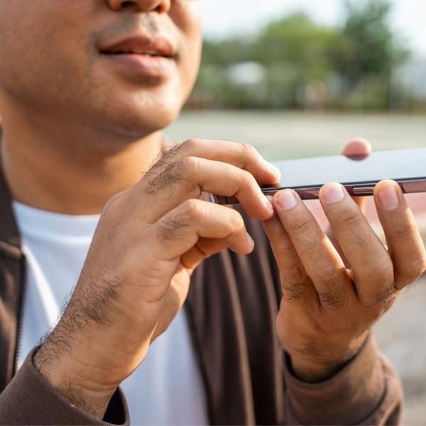 Person holding a smartphone and speaking into it, demonstrating voice interaction with a mobile device outdoors.