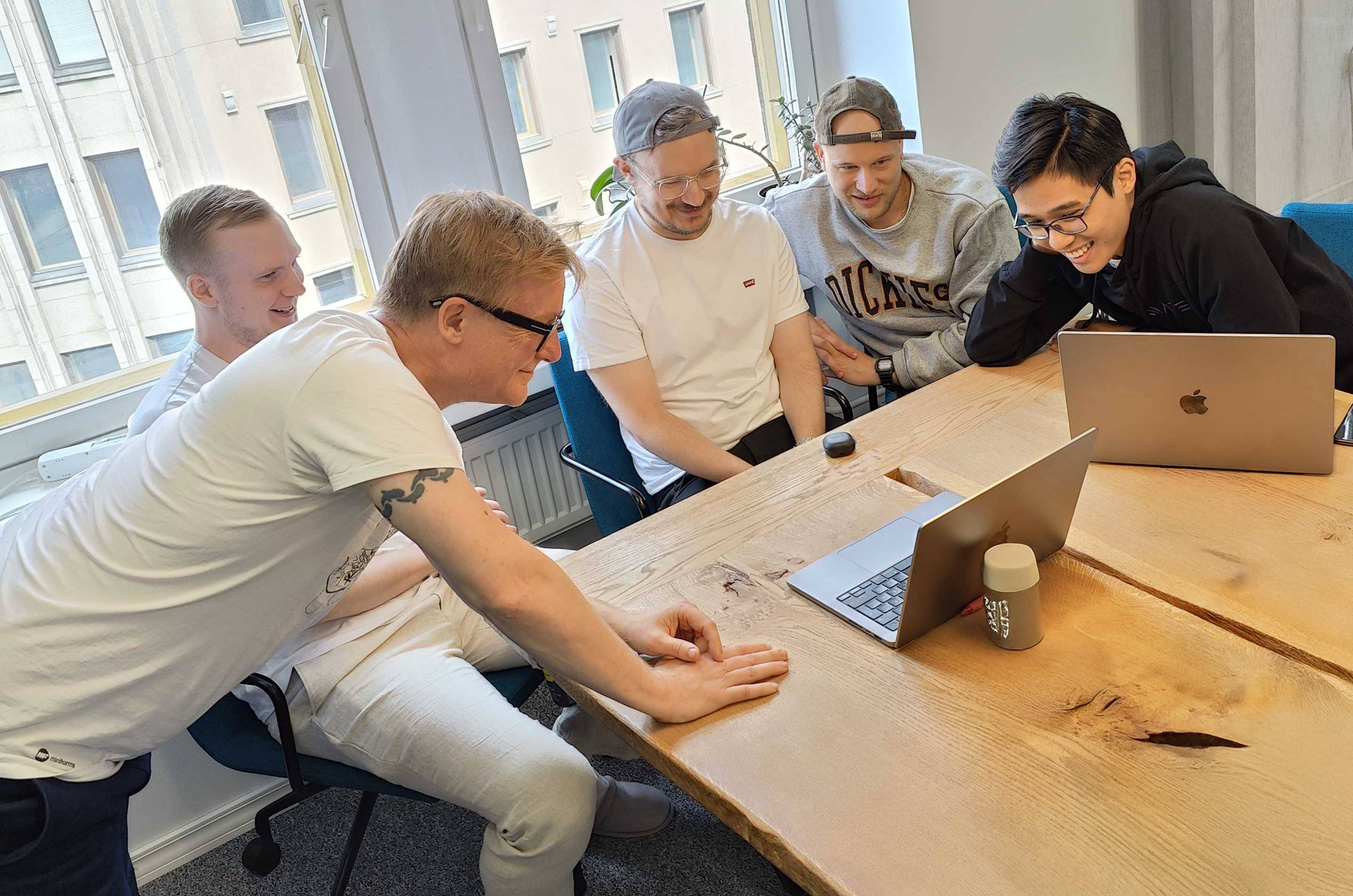 Four men around the wooden table looking at the computer, smiling.