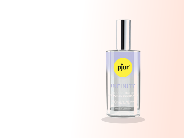 A tall Pjur Infinity silicone-based personal lubricant bottle stands large and unmistakable on a warm white-to-coral gradient, its long soft shadow reading like the last light of an unhurried evening.