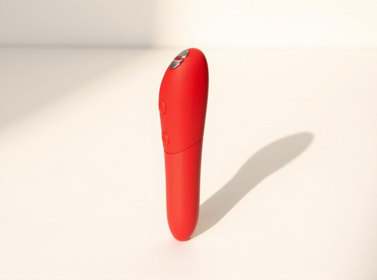 We-Vibe Tango X cherry bullet vibrator standing upright in warm daylight on a white surface, a simple beginner-friendly pick for easing first-toy overwhelm