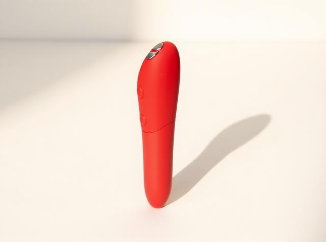 We-Vibe Tango X cherry bullet vibrator standing upright in warm daylight on a white surface, a simple beginner-friendly pick for easing first-toy overwhelm