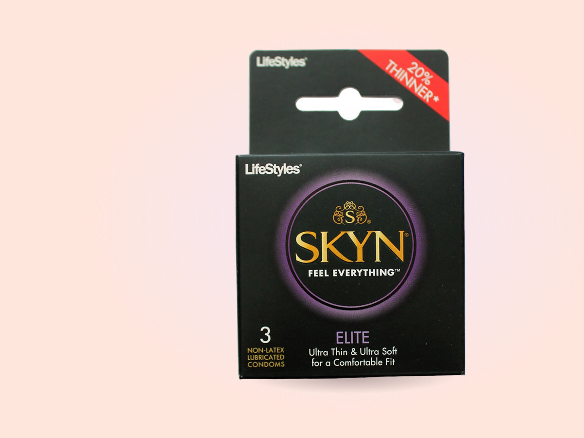 The SKYN Elite ultra-thin polyisoprene condoms box stands boldly on a warm coral backdrop, the material this guide recommends reaching for first.