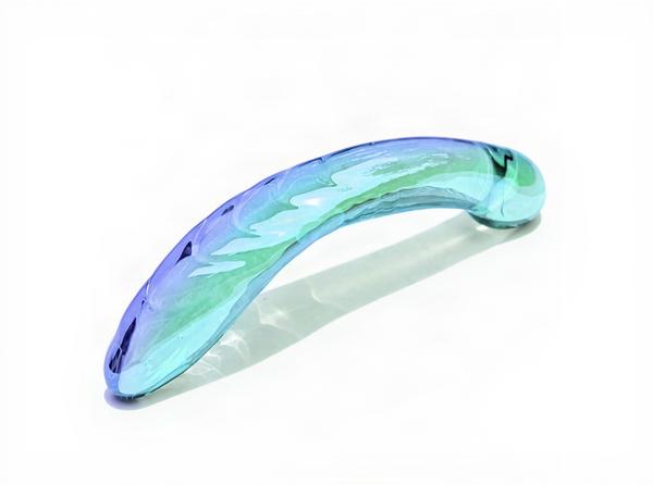 The Biird Kalii glass G-spot dildo, a curved borosilicate piece with an iridescent blue-violet to seafoam-green finish, resting on a bright white daylight surface, its smooth glossy surface catching clean highlights to show the non-porous material up close.