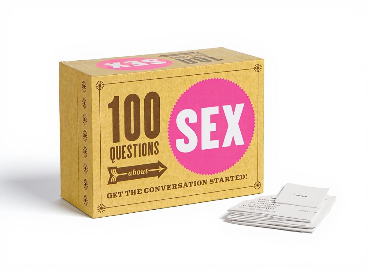 The 100 Questions About Sex conversation card game, its box standing upright with a few cards fanned beside it in warm daylight on a plain paper surface.