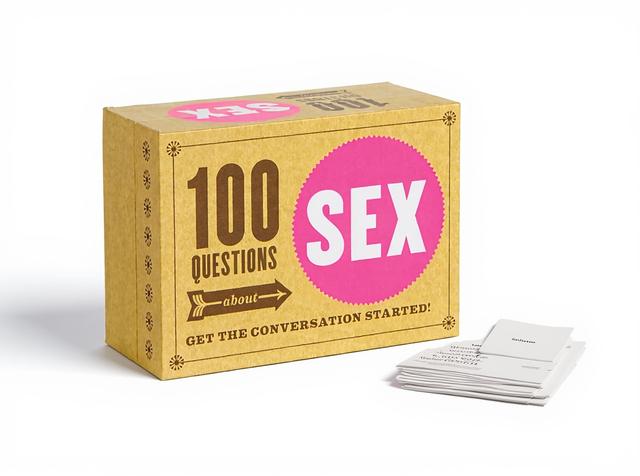The 100 Questions About Sex conversation card game, its box standing upright with a few cards fanned beside it in warm daylight on a plain paper surface.