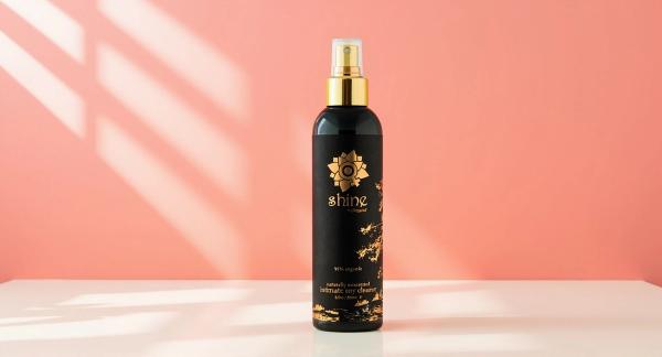 Sliquid Shine organic toy cleaner spray bottle standing on a sunlit counter in warm coral daylight, ready for a quick clean after every use