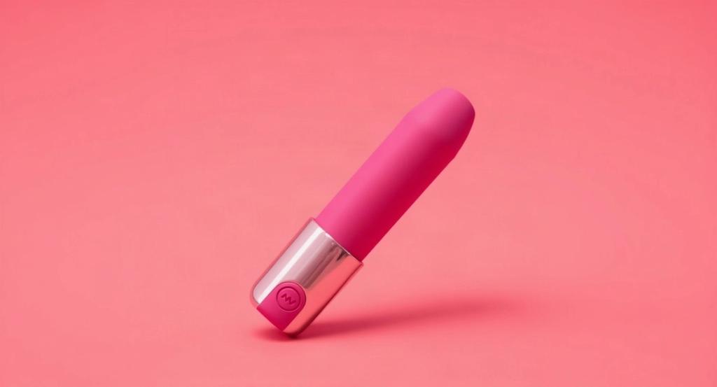 A slim rose ombre lipstick-style bullet vibrator shown large on a soft coral studio background in bright daylight.