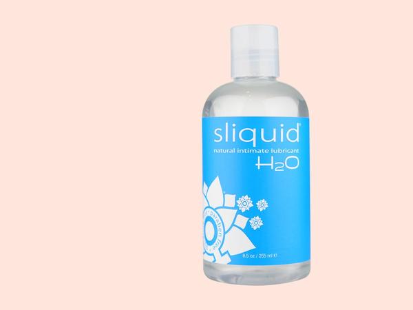 Sliquid Naturals H2O water-based lubricant standing boldly against a soft coral backdrop, the water-based pick in a water-versus-silicone-versus-hybrid lube comparison.