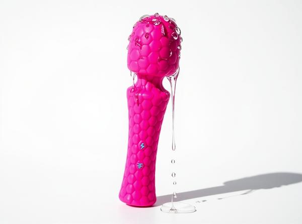 A hot-pink FemmeFunn Ultra Wand vibrator standing upright on a bright white background, freshly rinsed, with clear water droplets beading across its textured silicone head and catching the light after cleaning.