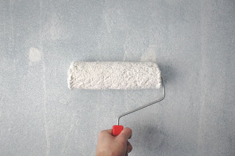 A roller covered in white paint being held against a semi-textured wall