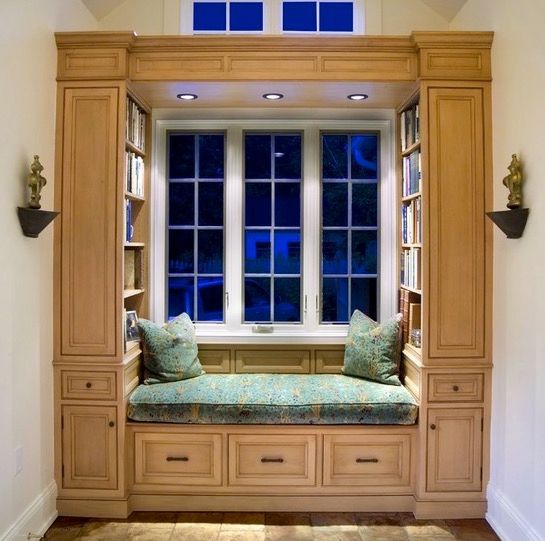 Light maple colonial-style built-in reading nook with book shelves, a green floral bench, matching throw pillows, and pot lights above 