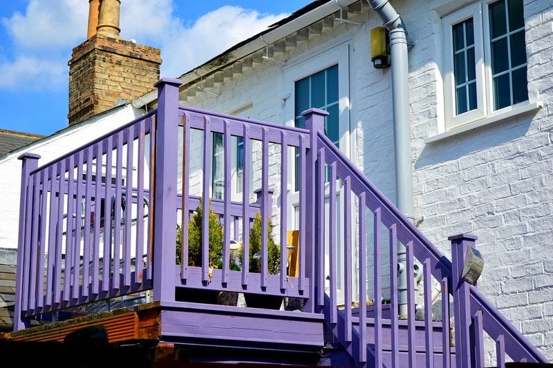 A white house with a deck and stairs that have been painted purple