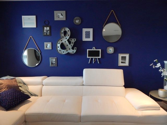 A white sofa with a navy painted wall behind it, displaying different sized frames, signs, and mirrors