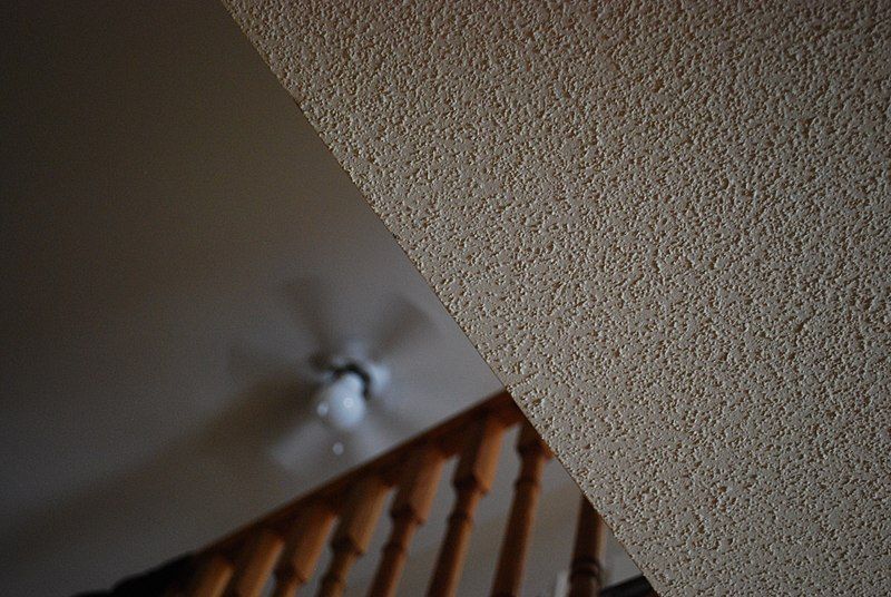 A closeup of a popcorn ceiling with a light shining in a dim room