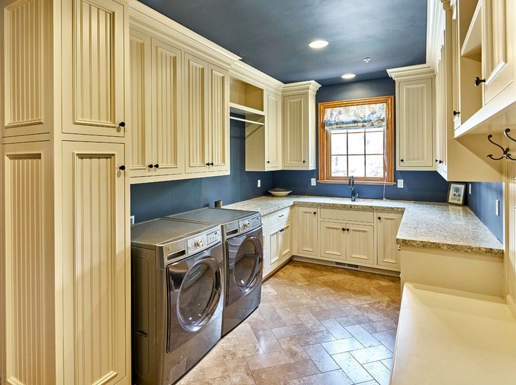 Blue painted laundry room with washer and dryer nestled into butter yellow upper and lower cabinetry