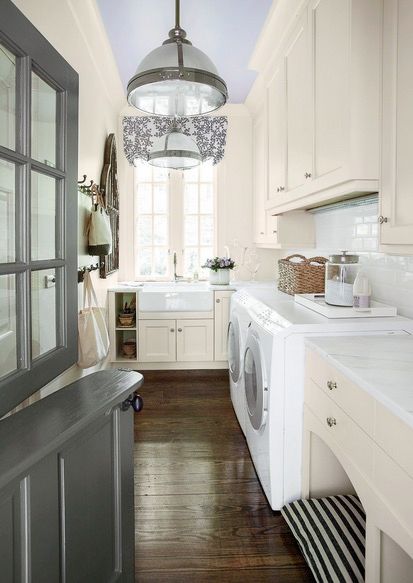 Laundry room with dark hard wood floor, soft beige upper and lower cabinetry, white washer and dryer, and polished nickel pendant lights
