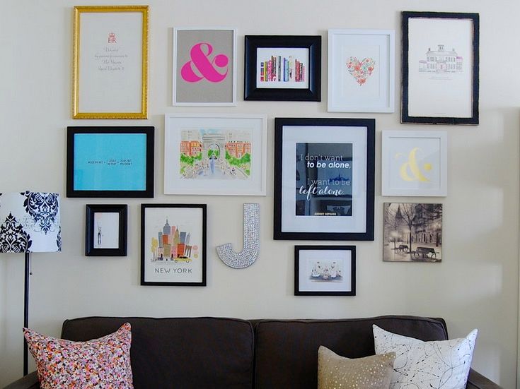 Photos in different sized and coloured frames hung on a gallery-style wall behind a black sofa with throw pillows