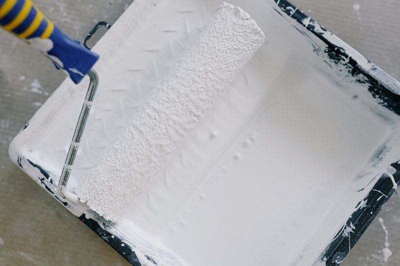 A closeup of a roller in a paint tray filled with white paint