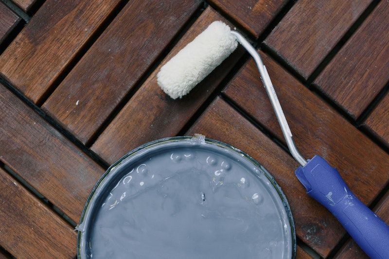 A roller on a wooden floor next to a paint can lid