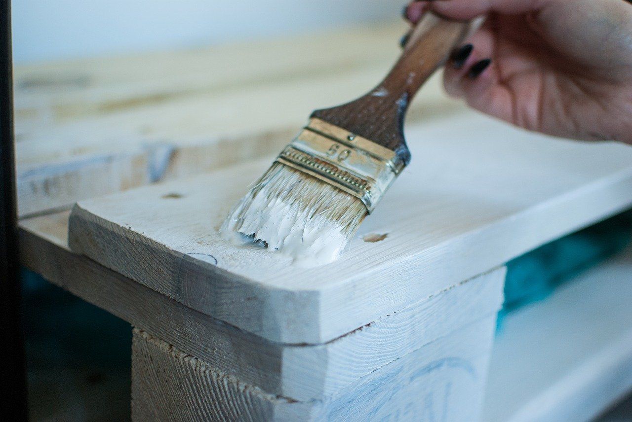 A closeup of a brush applying white paint to a shelf