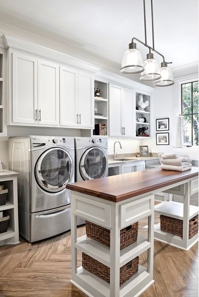 Laundry room with stainless steel washer and dryer and plenty of storage (upper white cabinets, island with storage below and folding counter on top)